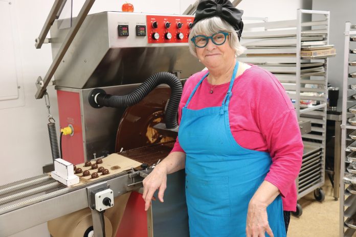 Chocolat Céleste owner Mary Leonard adds a layer of chocolate to truffles at her Midway facility. Leonard battled breast cancer in 2020, but didn’t miss a day of work. She had chocolates to create, after all. Each chocolate is hand made with fresh whipping cream, small batch butter and the finest fair trade cocoas. The company that she started at age 46 was named after her beloved Bichon Frise. (Photo by Tesha M. Christensen)